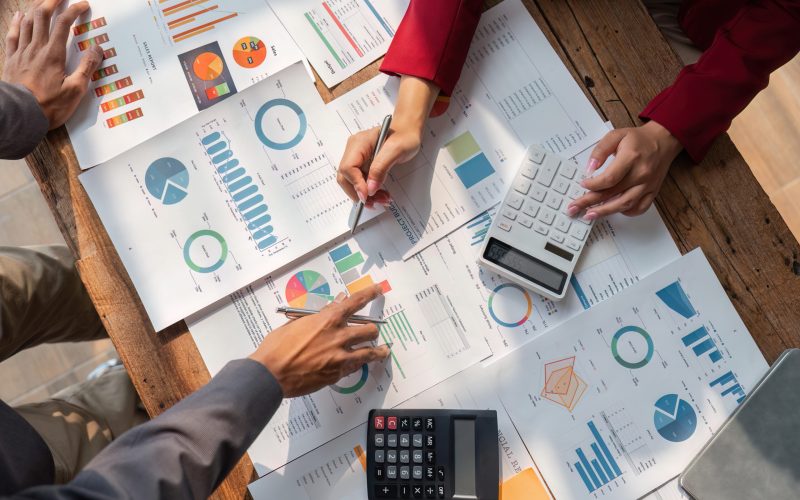 Business people brainstorming at office desk analyzing financial reports and pointing out financial data on a sheet, top view.